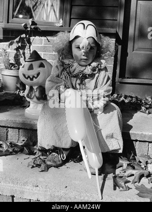 70 ENFANT DANS Trick or Treat COSTUME CLOWN ASSIS SUR PORTE AVANT L'ÉTAPE HOLDING BALLOONS Banque D'Images
