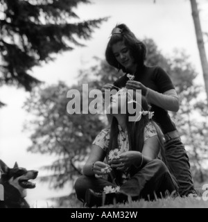 1970 DEUX FILLES Hippie de l'adolescence à l'extérieur assis dans l'HERBE L'UN EST DE METTRE DES FLEURS DANS LES CHEVEUX D'AUTRES Banque D'Images