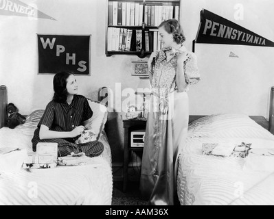 Années 1940 Années 1930 DEUX ADOLESCENTES DANS LA RÉGION DE COLLEGE DORM ROOM OUVERTURE PRÉSENTE SUR LE MUR des fanions 2 LITS DORTOIR Banque D'Images