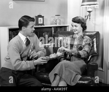 1950 Garçon Fille YOUNG TEEN COUPLE SITTING IN CHAIR Boire du coca EATING POTATO CHIPS Banque D'Images