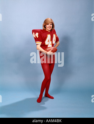 1970 WOMAN SMILING PORTER TRÈS GRAND FOOTBALL JERSEY ROUGE-ROUGE JUSTAUCORPS TENIR DEBOUT FOOTBALL fond bleu 44 Banque D'Images