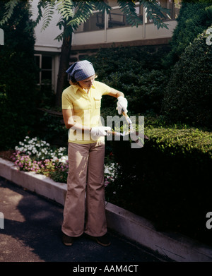 Femme des années 70, à l'aide d'un coupe-haie jardin de buis USURE BELLBOTTOMS Banque D'Images