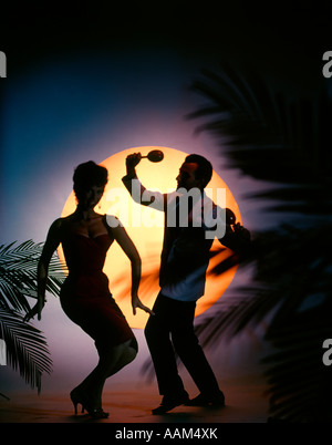 1970 MAN EN FACE DE PLEINE LUNE SUR LA PLAGE TROPICALE AVEC PALMIERS HOMME FEMME SILHOUETTE VACANCES MARACAS Banque D'Images
