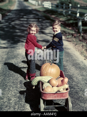 Années 1950 DEUX JEUNE ENFANTS Garçon Fille EN JEAN BLEU TIRANT RED WAGON plein de citrouilles et courges de récolte Banque D'Images