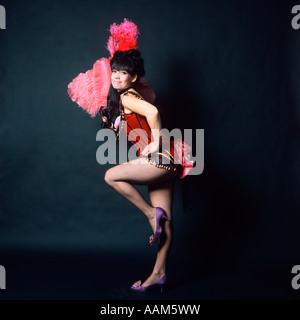 1960 American Woman in 1890s 1900s WILD WEST SALOON SHOWGIRL COSTUME STYLE AVEC PLUMES D'AUTRUCHE ROSE FAN LOOKING AT CAMERA Banque D'Images