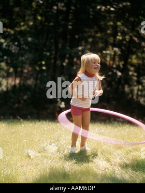 1960 Petite BLONDE GIRL PLAYING WITH Hula Hoop DANS UN ÉTÉ d'arrière-cour d'HERBE CHAUDE Banque D'Images