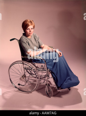 1960 PATIENT SMILING WOMAN SITTING IN WHEELCHAIR LOOKING AT CAMERA Banque D'Images