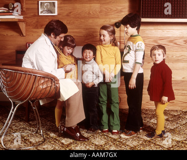 1970 1970 BLANC MANTEAU HOMME STEHOSCOPE MÉDECIN 5 enfants garçons filles asiatiques diversifié sur le bureau de médecins scolaires Banque D'Images