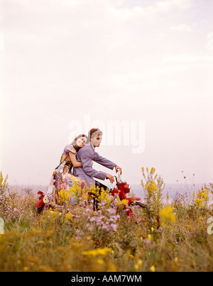 1970 1970 JEUNE COUPLE HOMME FEMME ROUGE ROMANTIQUE ÉQUITATION MOTO MOTO FLEURS CHAMP Banque D'Images