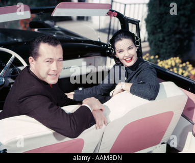 1950 SMILING COUPLE HOMME FEMME SUR LE SIÈGE AVANT se regarder en arrière rose et blanc SELLERIE CONVERTIBLE Banque D'Images