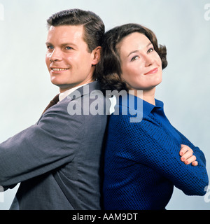 1960 SMILING MAN AND WOMAN STANDING WITH ARMS FOLDED SYMBOLIQUE STUDIO Banque D'Images