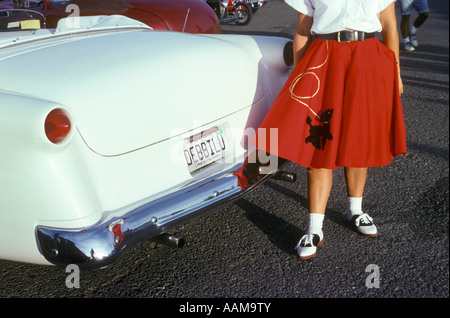 Femme EN ROUGE JUPE CANICHE ET CHAUSSURES DE SELLE À CÔTÉ DU BLANC 1950 Voiture Banque D'Images