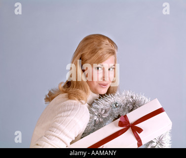 1970 1970 Femme blonde col roulé blanc SWEATER SMILING SEDUCTIVELY HOLDING BOX Red Ribbon & GERBE RETRO Banque D'Images