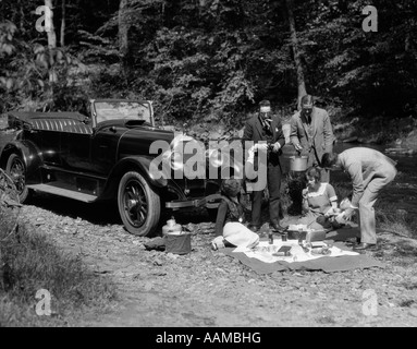 Années 20, GROUPE DE CINQ AVEC COUVERTURE ÉNONCÉS DANS L'AVANT DU CABRIOLET LE LONG DU CÔTÉ DE CREEK HAVING PICNIC Banque D'Images