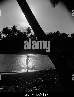 1940 Silhouette de femme debout sur la côte tropicale avec RAYON DE LUMIÈRE SUR L'EAU DERRIÈRE ELLE Banque D'Images