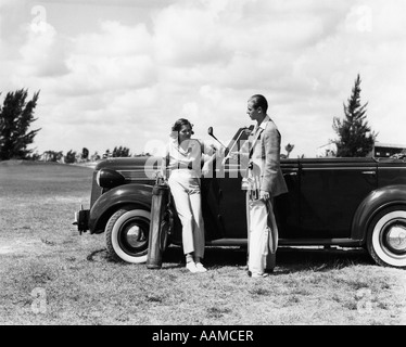 1930 DeSOTO CONVERTIBLE COUPLE LEANING ON PARLE AVEC DES SACS DE GOLF Banque D'Images