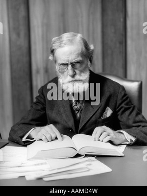 1930 HOMME ÂGÉ DANS LES VERRES SITTING AT DESK READING BOOK Banque D'Images