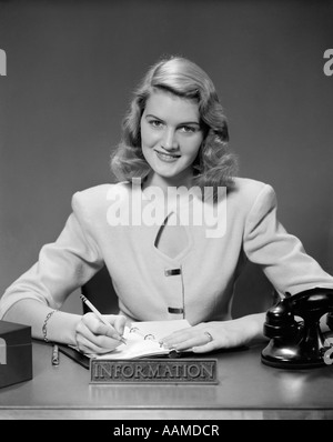 1950 WOMAN SITTING AT DESK IN OFFICE DE L'INFORMATION ÉCRIT DANS CARNET DE RENDEZ-VOUS Banque D'Images