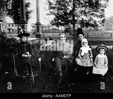 Années 1900 DÉBUT DU SIÈCLE FAMILLE DE SIX ASSIS DANS LA COUR AVANT AVEC UNE FILLE SUR TRICYCLE à l'ANCIENNE Banque D'Images