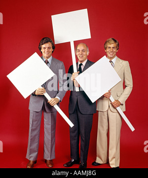 1970 1970 3 La FIGURE PLEINE D'AFFAIRES HOLDING BLANK SIGNS POSTERS AFFICHES FOND ROUGE HOMME HOMMES rétro d'affaires Banque D'Images
