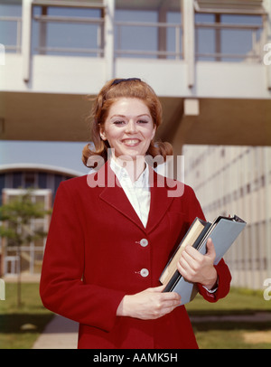 1960 TEEN GIRL HOLDING BOOKS PORTER BLAZER ROUGE SMILING AT CAMERA DEBOUT SUR LE CAMPUS HIGH SCHOOL Banque D'Images