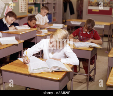 1960 LES ENFANTS DE L'ÉCOLE ÉLÉMENTAIRE DANS UN BUREAU À CLASSROM TRAVAILLER AVEC LES PAPIERS ET LES LIVRES Garçon Fille Banque D'Images