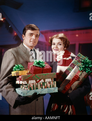 1960 1960 1970 1970 HOMME FEMME COUPLE HOLDING STOCK REMET DES PRÉSENTS EN FACE DE MAISON DÉCORÉE AVEC DES LUMIÈRES RETRO STUDIO Banque D'Images