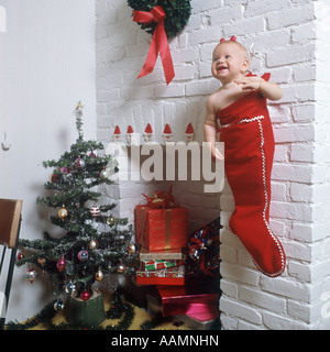 Peluche bébé fille en chaussettes accroché près de cheminée entourée de PRÉSENTE ET L'ARBRE DE NOËL Banque D'Images