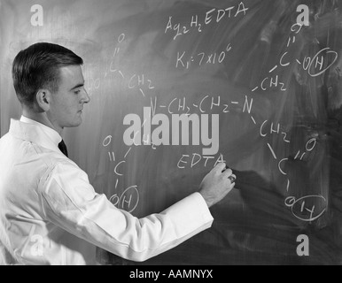 1960 PROFIL DE L'HOMME SCIENTIFIQUE IN LAB COAT de l'ÉCRITURE D'une formule chimique SUR TABLEAU NOIR Banque D'Images