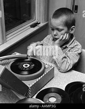 1970 GARÇON AVEC BUZZ COUPE DE MENTON DANS LA MAIN ASSIS À TABLE À ÉCOUTER DE LA MUSIQUE SUR PORTABLE petit disque 45 tours Banque D'Images