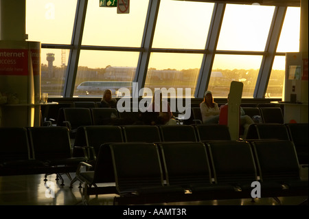 Quelques autres passagers assis à ne pas fumer zone de départ de l'aéroport international de Dublin en Irlande, la lumière du soir Banque D'Images