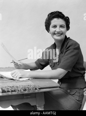 Années 1930 Années 1940 Femme assise AU BUREAU AVEC DES PAPIERS ET UN CRAYON LOOKING AT CAMERA Banque D'Images