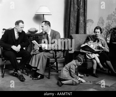 1930 DANS LA SALLE DE SÉJOUR FAMILLE PAPA MAMAN PARLE VENDEUR D'ASSURANCE PRÉSIDENT TRICOT FILLE FILS JOUANT SUR MARBRE Banque D'Images