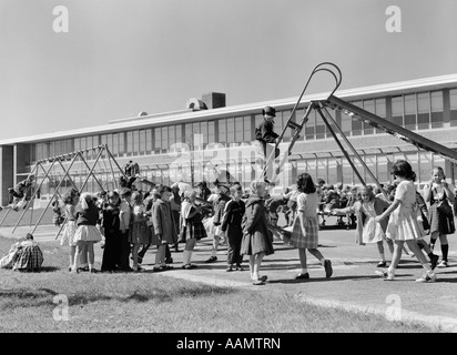 1950 AIRE DE JEUX DE L'ÉCOLE ÉLÉMENTAIRE À LA RÉCRÉATION AVEC DES ENFANTS QUI JOUENT SUR LA DIAPOSITIVE ET SWING SET Banque D'Images