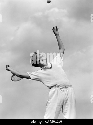 Années 1930 Années 1940 GARÇON TENNIS PLAYER THROWING BALL DANS L'AIR POUR SERVIR AVEC UNE RAQUETTE DE TENNIS DANS LA MAIN Banque D'Images