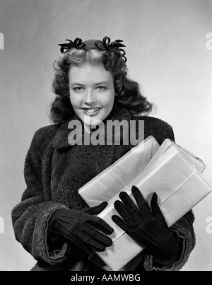 1940 SMILING YOUNG WOMAN WEARING COAT GANTS ET CHAPEAU AVEC ARCS TRANSPORTANT DES PAQUETS ENVELOPPÉS LOOKING AT CAMERA Banque D'Images