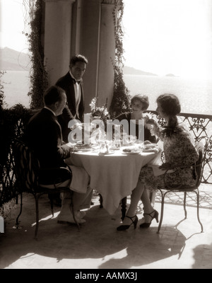 1920 MANGER SUR BALCON AVEC GROUPE WAITER SERVING WINE Banque D'Images