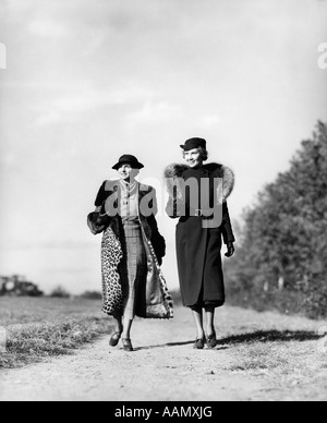 1930 DEUX FEMMES marchant sur une route rurale Porte manteau de fourrure LÉOPARD DE L'AUTRE PORTANT MANTEAU AVEC Étole de fourrure OUTDOOR Banque D'Images