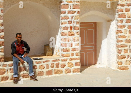 Troglodyte berbère homme est assis dans l'abri de l'ombre dans la cour de sa maison familiale sous terre en séjour à Matmata Tunisie Banque D'Images