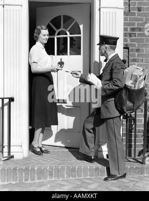 1930 POSTMAN DONNANT UNE LETTRE À UNE FEMME DANS L'embrasure D'UNE MAISON EN BRIQUE COLONIALE Banque D'Images