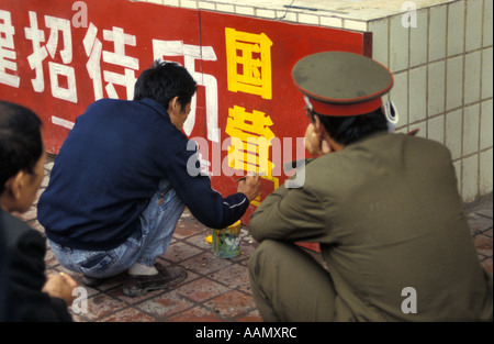 Artiste chinois peint calligraphie publicité sur la rue de Xian, étant négligé par l'officier de l'armée accroupie, Shaanxi, Chine Banque D'Images