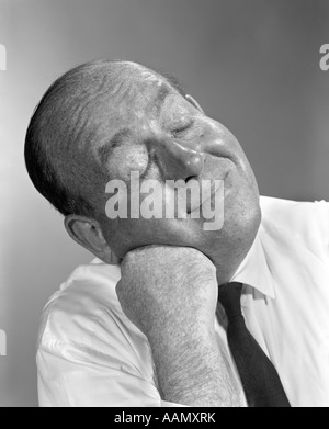 Années 1950 Années 1960 BALDING MAN LEANING HEAD ON FIST en chemise et cravate yeux fermés SMILING EXPRESSION PENSÉE Banque D'Images