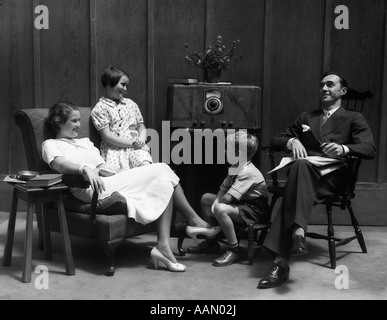 1930 homme de famille Père Mère FEMME Fille Garçon Fille FILS DANS LA SALLE DE SÉJOUR SE SONT RÉUNIS AUTOUR DE L'ÉCOUTE DE LA RADIO Banque D'Images