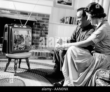 1950 COUPLE MARI ET FEMME REGARDANT LA TÉLÉVISION DANS LE SALON INTÉRIEUR SMILING Banque D'Images