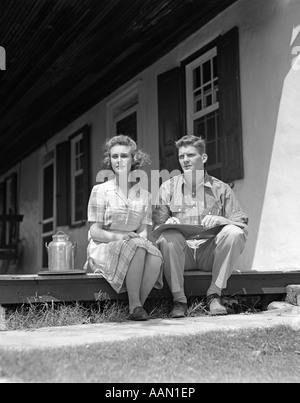 1940 HOMME FEMME COUPLE ASSIS À LA MAISON FERME PORCHE DE CÔTÉ GRAND LIVRE LES GENOUX de l'homme petite robe à carreaux Femme du réservoir de lait Banque D'Images