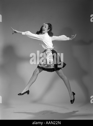 1960 FEMME AU FOYER FEMME PORTER DANS L'AIR DE SAUT SAUT TABLIER jupe noire chemisier blanc HAPPY SMILING JOIE DINGO CARACTÈRE EXPRESSION LOUFOQUE Banque D'Images