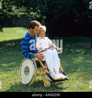 Homme handicapé en fauteuil roulant lisant un livre à un petit garçon dans le jardin Banque D'Images