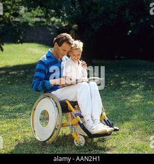 Homme handicapé en fauteuil roulant lisant un livre à un petit garçon dans le jardin Banque D'Images