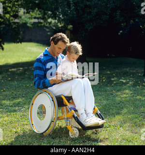 Homme handicapé en fauteuil roulant lisant un livre à un petit garçon dans le jardin Banque D'Images