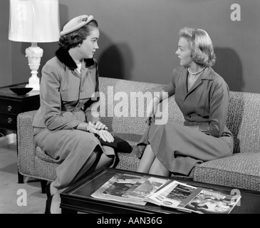 1950 PAIRE DE WOMEN SITTING ON SOFA DU SALON à parler l'un portant costume avec chapeau et gants Banque D'Images